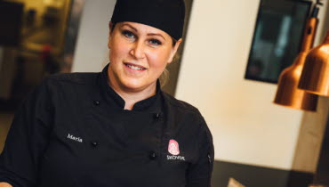 Person klädd i mörka arbetskläder serverar ett fat med mat.